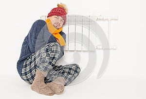 Man feeling cold in hat and pullover sitting close to radiator. Gas crisis concept