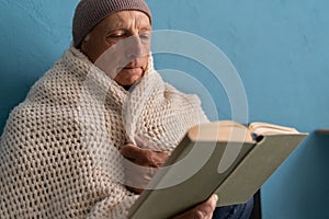 Man feeling cold at home with home heating trouble, he reads book sitting on bed, close-up. Concept of no heating