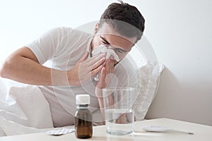 Man feeling cold, lying in the bed and blowing his nose