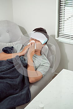 Man feeling cold, lying in the sofa and blowing his nose