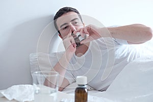 Man feeling cold and using a nasal spray lying in the bed