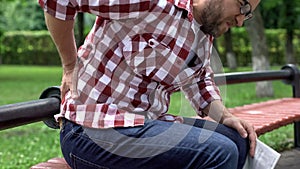 Man feeling lower back pain, reading newspaper in park, compressed nerve roots