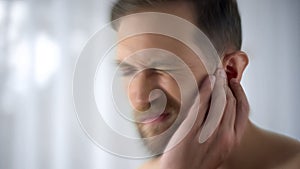 Man feels pain in middle ear, meningitis and hearing loss, inflammation, closeup photo