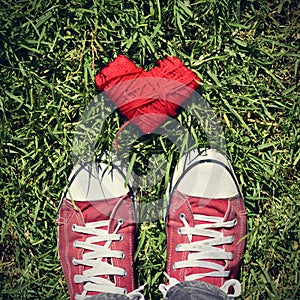 Man feet and heart-shaped coil of red cord on the grass, vignett