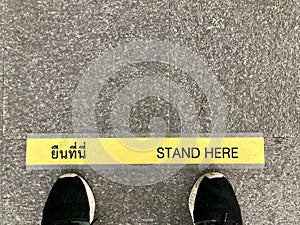 A man Feet standing behind the â€œStand hereâ€ yellow line. The Thai word in this photo is mean â€œStand Hereâ€.
