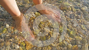 Man Feet Standing In Very Clear Ocean Water, Sea Water. Man Legs covered with water with visible buttom. Tourist legs in