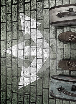 Man feet in suede boots. Vintage suitcases stand on paving stone road. White arrows point  three different directions.