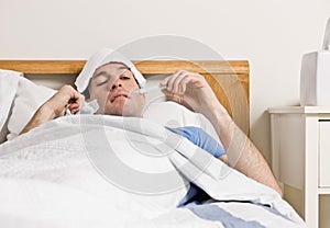 Man with fever laying in bed taking temperature