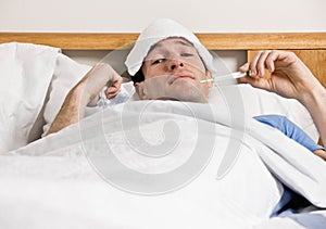 Man with fever laying in bed taking temperature photo