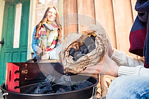 Man filling grill with charcoal near smiling woman