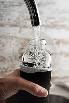 Man filling a reusable water bottle from a tap