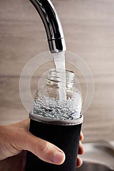 Man filling a reusable water bottle from a tap