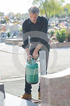 Man filling watering can in graveyard