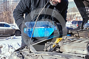 Man filling a windshield washer tank of a car by antifreeze