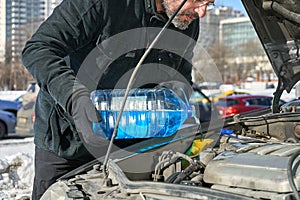 Man filling a windshield washer tank of a car by antifreeze on busy Moscow street in winter