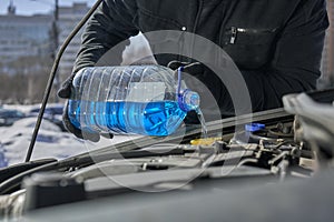 Man filling a windshield washer tank of a car by antifreeze