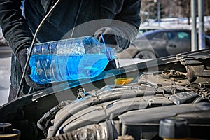 Man filling a windshield washer tank of a car by antifreeze