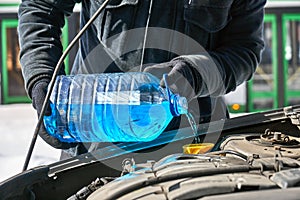 Man filling a windshield washer tank of a car by antifreeze in winter outdoors