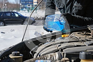 Man filling a windshield washer tank of a car by antifreeze on winter Moscow street