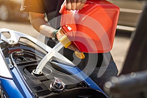 Man fills the fuel into the gas tank of motorcycle from a red canister or plastic fuel can .maintenance repair motorcycle concept