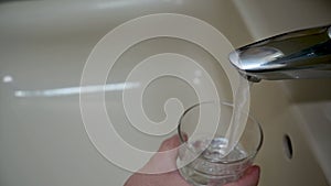 Man fills a glass with water from the bathroom sink.