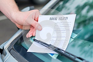 Man finding a ticket fine under the car windscreen because of parking violation