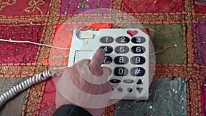 Man finger pressing numbers buttons on classic telephone on colorful tablecloth