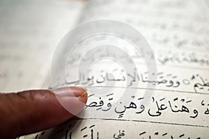 A man fingerpointing to the words in Arabic, in the Qur'an