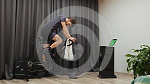 Man finished cycling training on stationary smart bicycle trainer. Young male cyclist turns off cycling computer and stops pedalin