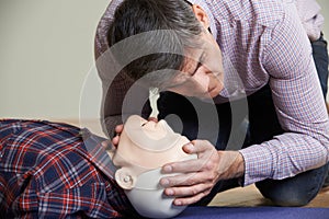 Man In First Aid Class Checking Airway On CPR Dummy