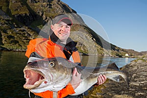 Man in a fisherman`s cap holding a big fish cod. Smiling