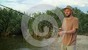 a man fisherman at sunset in a hat on the lake catches fish with a fishing rod against the background of reeds. stands