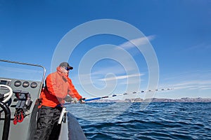 Man fishing from a boat fishing rod. Red Jacket.