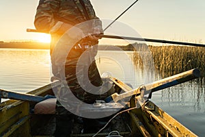 A man is fishing from a boat on sunset