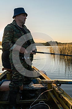 A man is fishing from a boat on sunset