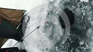 Man fishing in ice hole. Fisherman with fishing rod catching fish.Vertical video