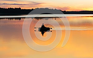 Man fishing on lake from boat at sunset or sunrise time. Fisherman silhouette at sunset