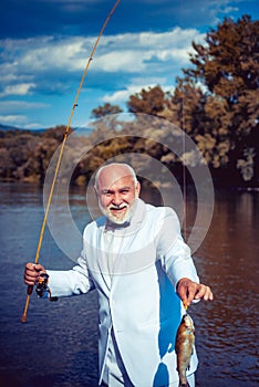 Man fishing on the lake. With fish. Summer vacation. Retired mature bearded male human in suit. Brutal man stand in