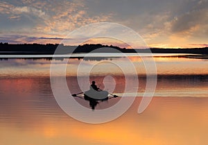 Man fishing on lake from small rowing boat at sunset or sunrise time. Fisherman silhouette at sunset