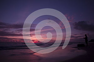 Man fishing in ocean from beach on sunset