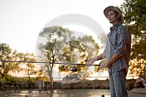 Man fishing outside in evening on lake in summer, enjoy spending time in nature, side view portrait of male in casual