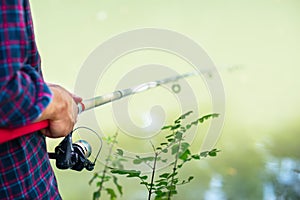 Man fishing at river bank, summer outdoor. Summer leisure, hobby. Fishing. Angling. Man`s hand with fishing rod over light green