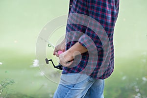 Man fishing at river bank, summer outdoor. Summer leisure, hobby. Fishing. Angling. Man`s hand with fishing rod over light green