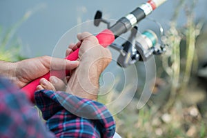 Man fishing at river bank, summer outdoor. Summer leisure, hobby. Fishing. Angling. Man`s hand with fishing rod over light green