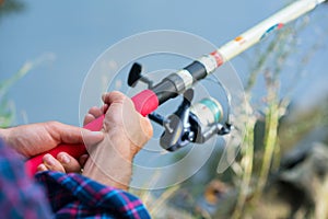 Man fishing at river bank, summer outdoor. Summer leisure, hobby. Fishing. Angling. Man`s hand with fishing rod over light green