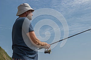 man with a fishing rod in his hands against the blue sky