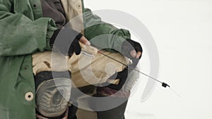 Man with fishing rod on lake in winter, close up shot. Fisherman is fishing in ice hole. Winter fishing concept. Winter extreme eq