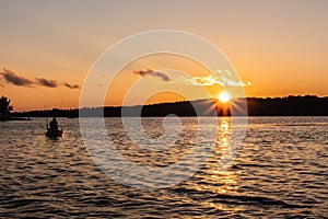 a man fishing at sunset on a lake near trees and mountains