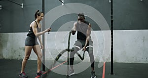 Man, fitness and personal trainer with battle ropes for exercise, workout or training at gym. Active woman or coach