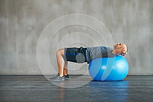 Man, fitness and stretching with exercise ball for workout, training or balance at gym. Active male person lying on